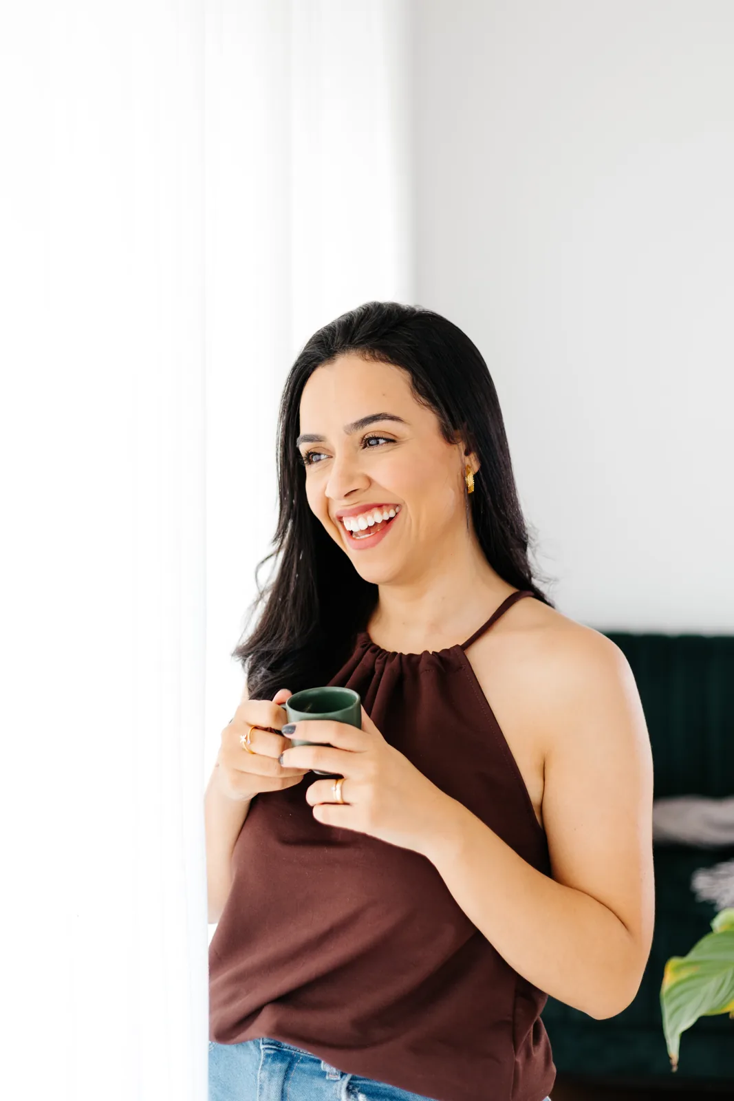 Nanda junto à janela, sorrindo com uma caneca nas mãos